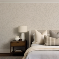 Neatly made bed with pillows against a wall with leaf-patterned wallpaper.
