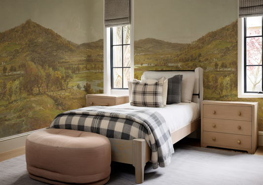 Bedroom with checkered blanket, pillows, and a beige ottoman in front of landscape wall art.