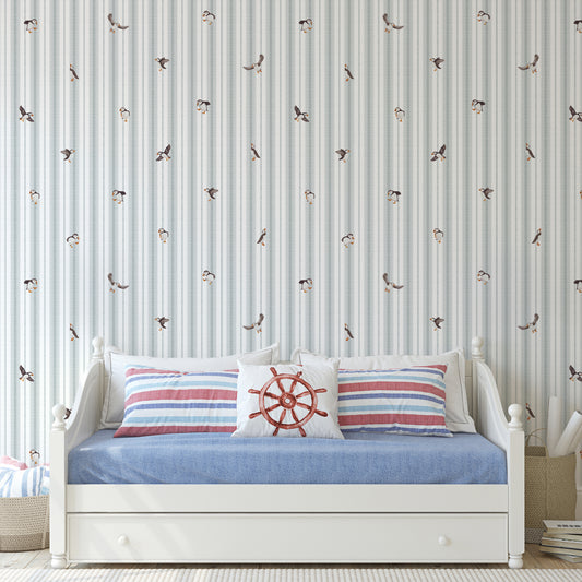 White bed with striped pillows against a wall with bird pattern