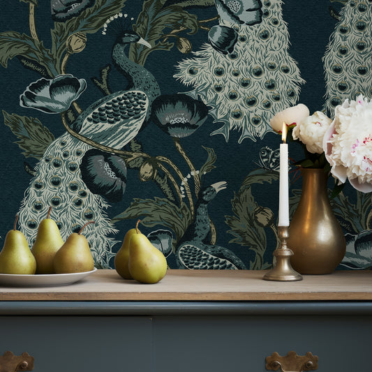 Decorative peacock wallpaper with pears, a candle, and a vase on a wooden surface.