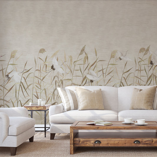 A styled living room featuring a large wall mural with a natural reed and bird pattern in beige and brown tones, behind a white sofa with neutral throw pillows and a wooden coffee table.