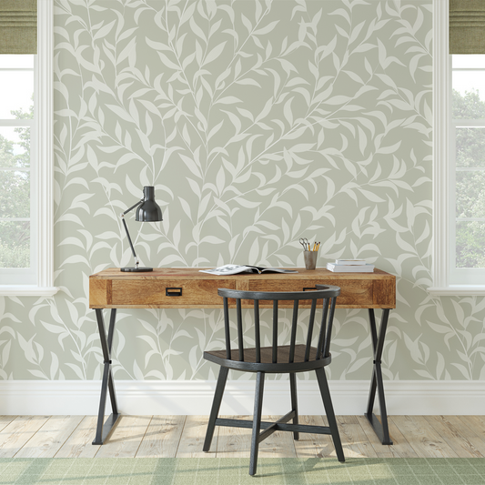 Wooden desk with black chair against a leaf-patterned wallpaper wall.